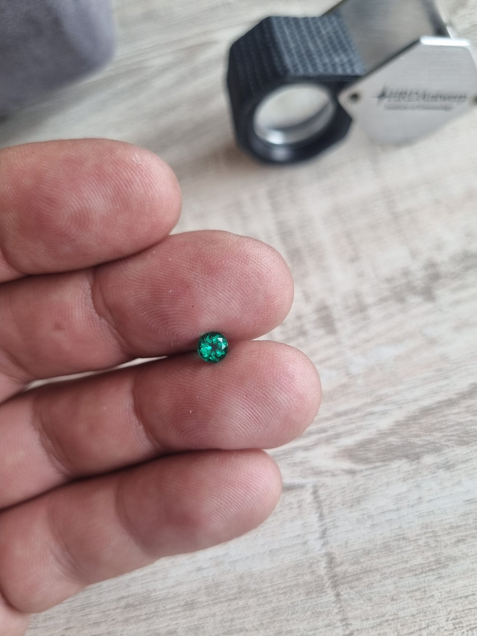 Émeraude taillée présentée près d’une loupe gemmologique