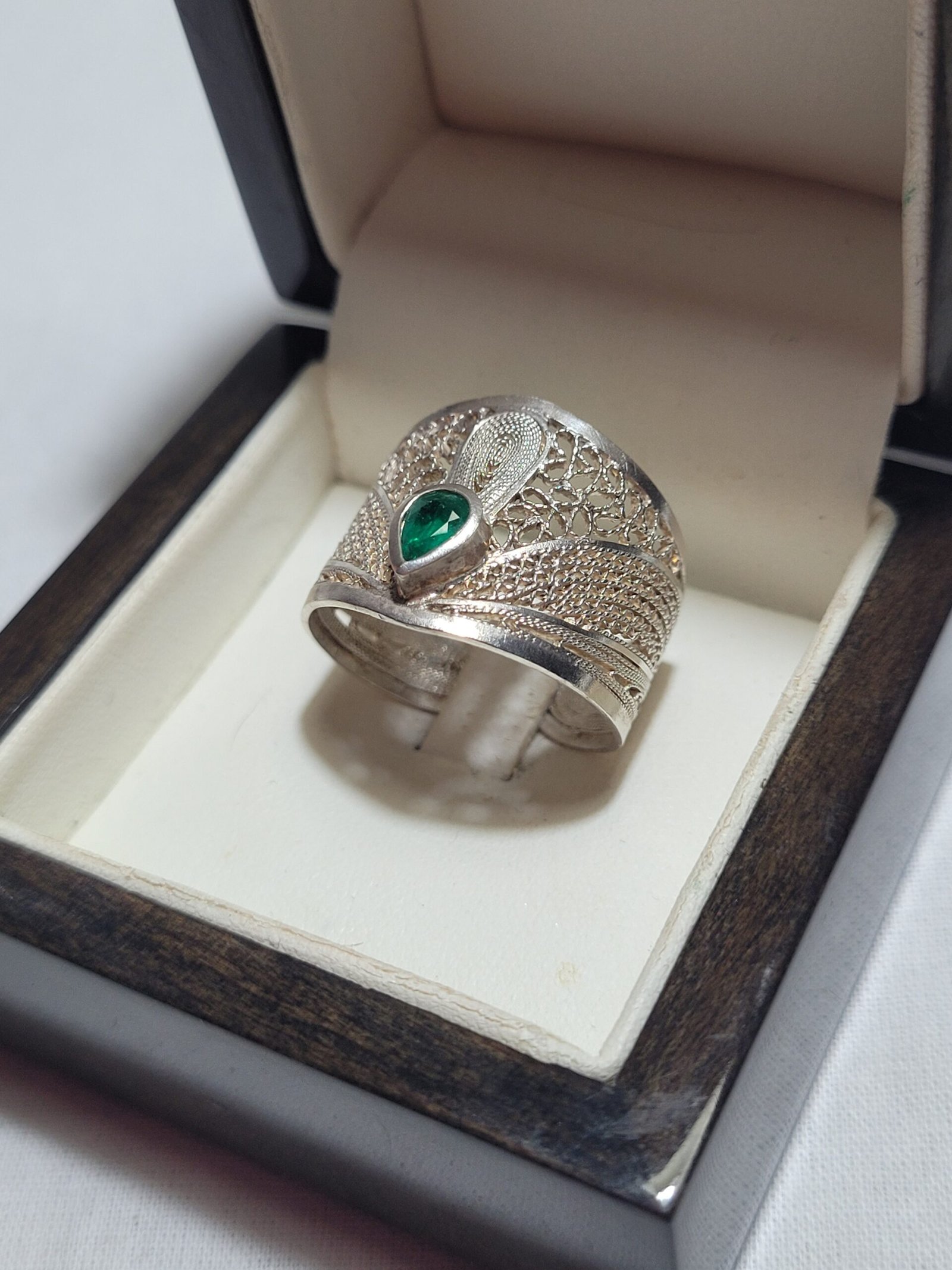 Bague ajourée en filigrane avec une émeraude en forme de poire, présentée dans son écrin